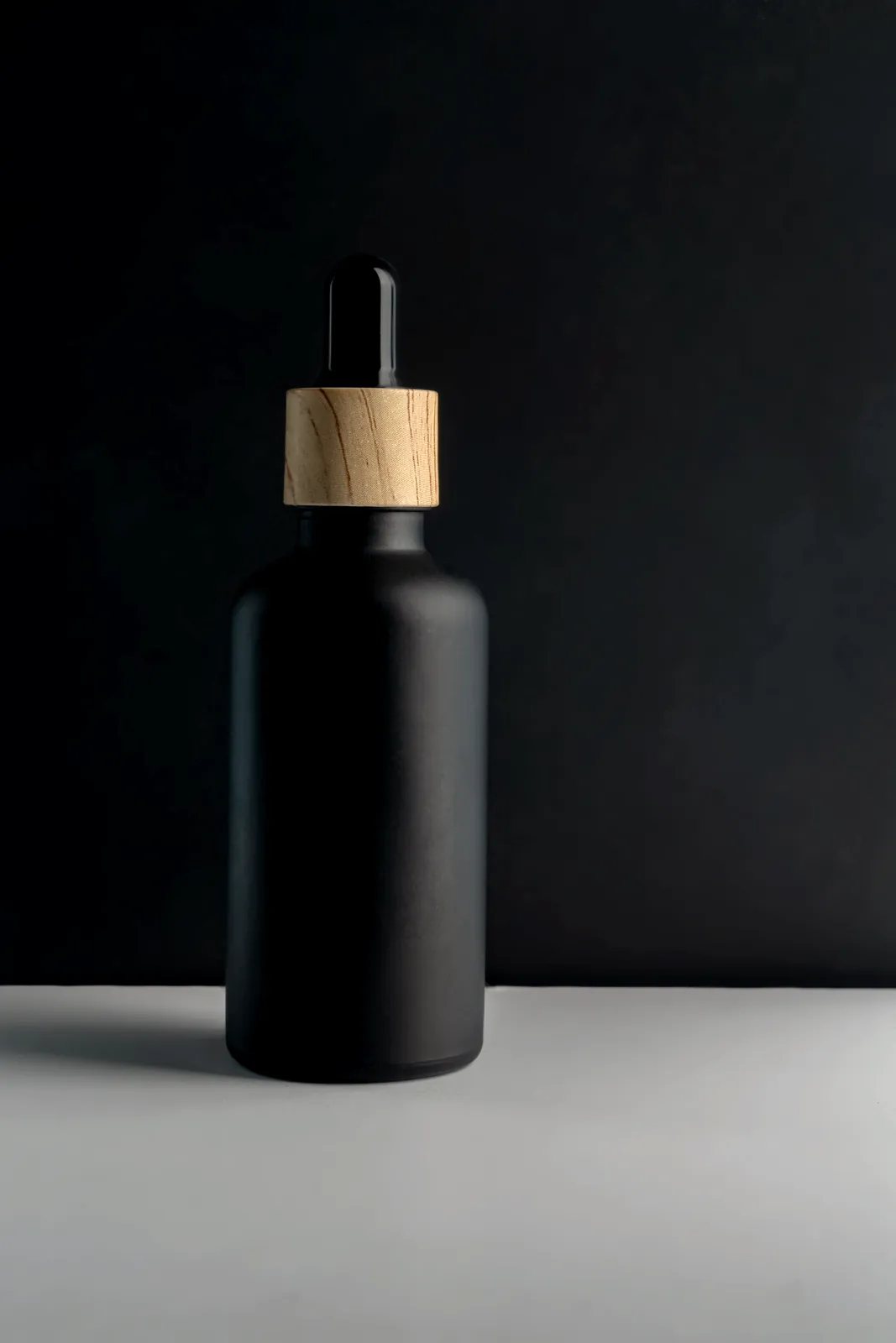 A black bottle with a wooden stopper on a pale surface.