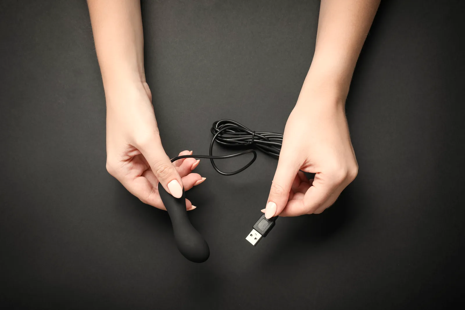 Hands holding a small black bullet and its charging cable.